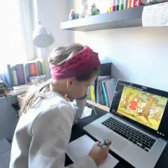 Dziewczynka w opasce na głowie uczy się zdalnie przy laptopie, oglądając bajkę.
