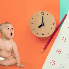 Zaskoczony niemowlak obok zegara i kalendarza.