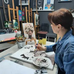 Kobieta w dżinsowej kurtce maluje obraz z kwiatami na płótnie w pracowni artystycznej.