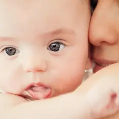 Zbliżenie na twarz niemowlaka z wyciągniętym językiem, przytulonego do matki.