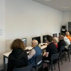 Grupa osób w różnym wieku uczy się obsługi komputera. To idealny przykład, co to zajęcia z samorozwoju dla każdego.
