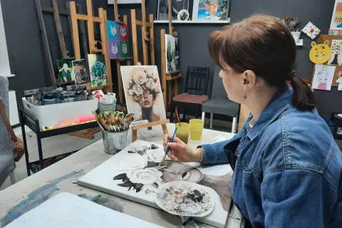Kobieta w dżinsowej kurtce maluje obraz z kwiatami na płótnie w pracowni artystycznej.