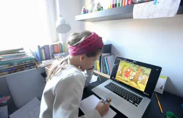 Dziewczynka w opasce na głowie uczy się zdalnie przy laptopie, oglądając bajkę.