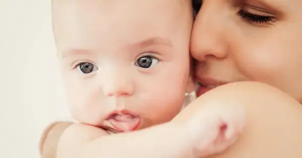 Zbliżenie na twarz niemowlaka z wyciągniętym językiem, przytulonego do matki.
